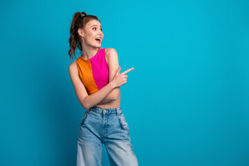 Young woman in fashionable summer outfit pointing with a joyful expression against a vibrant blue...