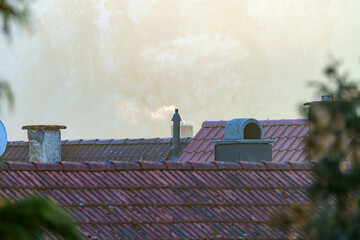 Rooftops with chimney details under a soft morning fog in a quiet urban landscape at sunrise