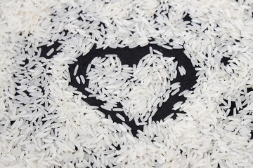 White rice grains with black background with a heart drawing in the middle