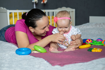 A mother and her adorable baby girl enjoy a playful afternoon on a cozy bed. They share smiles and...