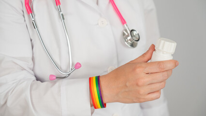 Close up of doctor's hand with rainbow bracelet holding medicine bottle. 