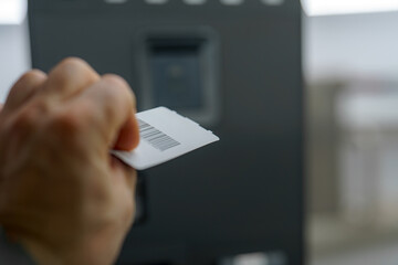 Hand holding a card near a card reader at a modern self-service kiosk in a public space during...