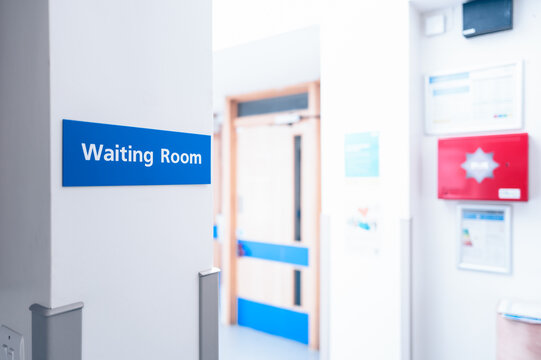 Shallow focus of a typical Waiting Room sign seen within a GP surgery and clinic. Various doctor's offices are through the door in the background. Seen just before the surgery is open to the public.