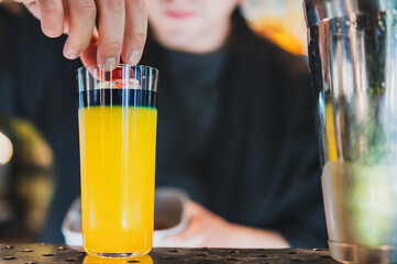 Bartender placing cherry in layered cocktail with vibrant blue and yellow colors. Close-up at bar...