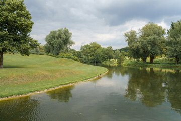 Calm riverbank with lush greenery and overcast sky in a serene landscape during late afternoon