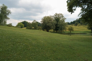 Peaceful landscape of green hills and trees near a calm pond on an overcast day in a rural area