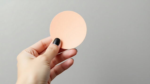 Woman's hand holding a peach-colored round paper mockup against a gray background.