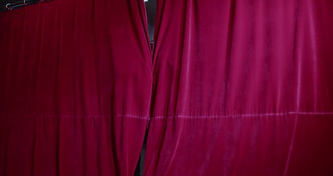Two young actors peek through a gap in the red stage curtains. They look surprised and excited to see the audience. Theatre, acting, and performance.