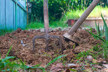 Close-up of freshly plowed earth with a pitchfork stuck upright in the soil and a hoe lying beside...
