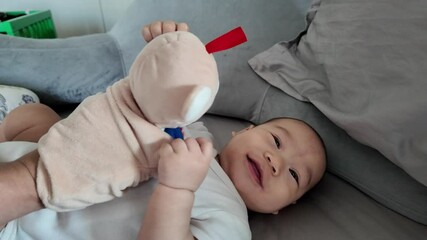 A happy baby smiles while playing with a soft plush toy. The child is comfortably seated, showcasing the joy of playful moments.