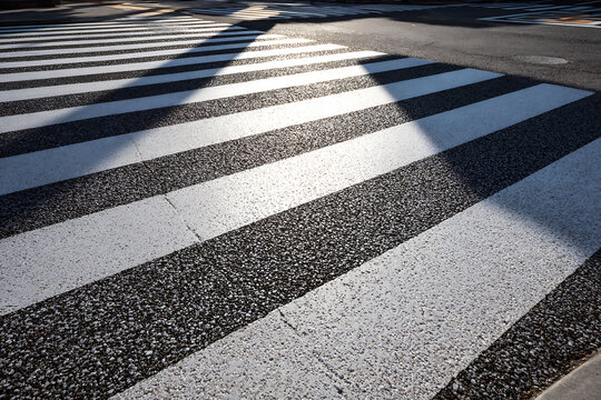Abstract pattern of sunlight and shadow on a pedestrian crossing on an asphalt road