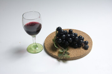 Glass of red wine and bunch of black grapes on a white background
