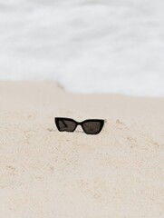 Editorial aesthetic Black cat-eye sunglasses on warm white beach sand, minimalist lifestyle for social media faceless digital content marketing