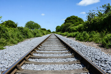 Perspective view of a railway track disappearing into the distance under a clear blue sky