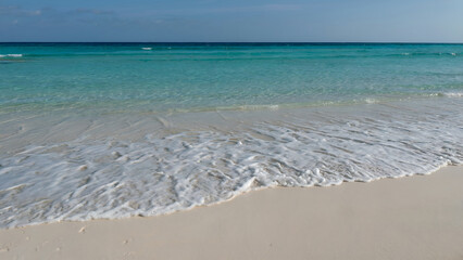Serene turquoise ocean waves gently lap onto a pristine white sand beach on a sunny, tropical day.