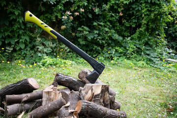 Fototapeta premium Outdoor scene with an axe embedded in a chopping block beside a pile of logs, suggesting rustic living, firewood preparation, or woodland work.