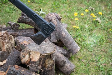 Outdoor scene with an axe embedded in a chopping block beside a pile of logs, suggesting rustic...
