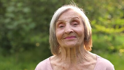 Close-up portrait of happy elderly woman with silver hair, over 80 years old, standing outdoors in the warm light of sunset. She smiles directly into the camera, radiating warmth, kindness experience