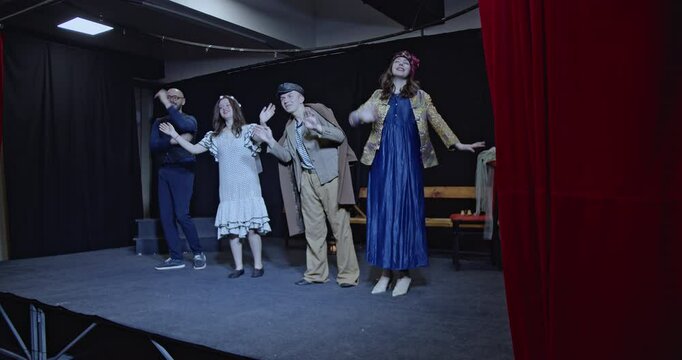 Young actors bow to their audience after a theater play. The actors take a bow and wave goodbye as they exit the stage.