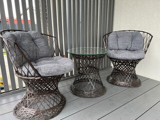 Metal chairs imitating rattan wicker furniture on the terrace of a modern house. Table with glass...