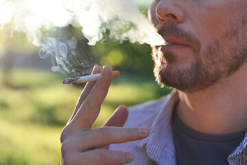 Man smoking cigarette on blurred background, closeup