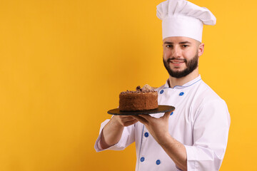 Happy confectioner in uniform holding chocolate cake on orange background