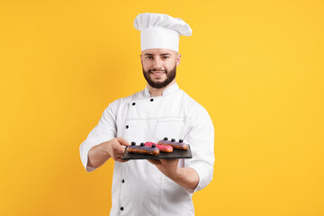 Happy confectioner in uniform holding eclairs on orange background