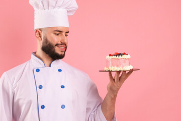 Happy confectioner in uniform holding cake with berries on pink background