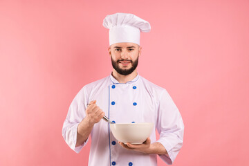Happy confectioner in uniform holding whisk and bowl on pink background