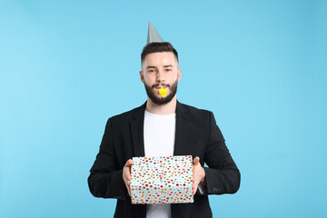 Happy Birthday. Handsome man with party hat, blower and gift box on light blue background