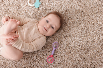 Cute little baby with rattle toy on floor at home, above view. Space for text