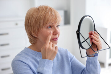 Senior woman putting on contact lenses near mirror in ophthalmologist office