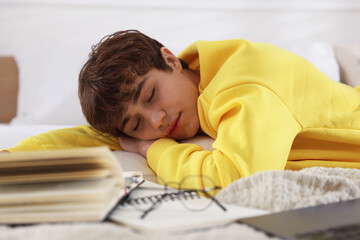Tired teenage student sleeping near books on bed at home