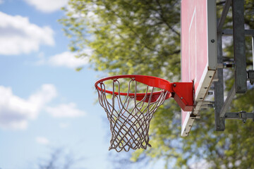 Basketball hoop outdoors, green tree and blue sky in the background