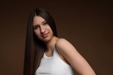 Portrait of beautiful teenage girl with healthy long hair on brown background