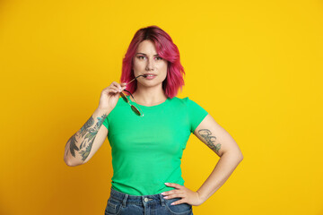 Beautiful woman with pink dyed hair and sunglasses on yellow background