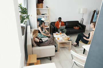 Young adult coworkers socializing and working together in a cozy workplace, featuring a woman...