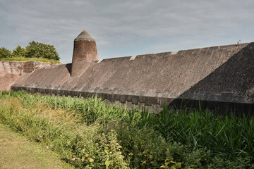 Historic brick fortification wall and tower surrounded by moat and greenery