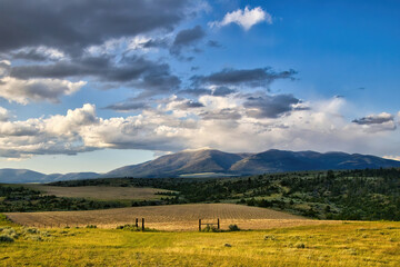 Landscape of distant mountains beyond a fenced in field on an overcast Summer day near Townsend in...