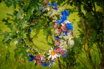 A close-up of a handmade wreath made of wildflowers and oak leaves hanging outdoors in a green...