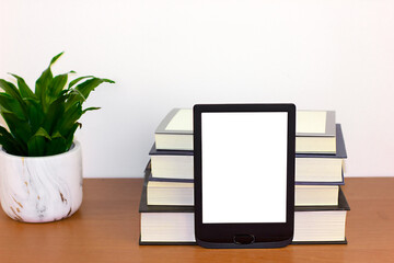 E-reader and books on a wooden desk with a plant