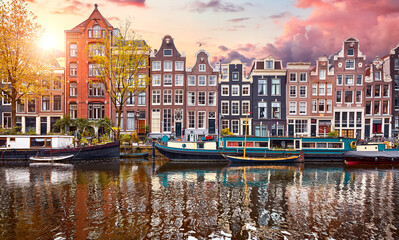 Amsterdam, Netherlands. Panorama of famous dancing houses on river Amstel, water channels with house boats. Popular landmark and travel destination in old european city. Evening sunset landscape.