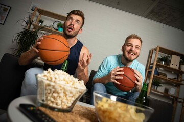Two emotional sports fans watching TV and eating snacks
