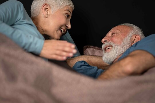Smiling senior couple having conversation while lying in bed