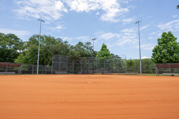Baseball field with orange dirt in a park under clear blue sky in midday light