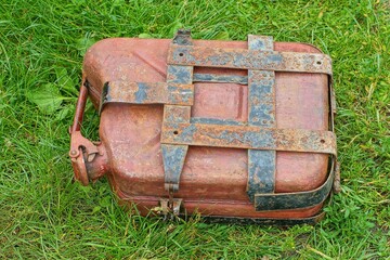 one closed lid retro brown with handle iron fuel industrial old motorcycle in case with plates canister lies on green grass day outside