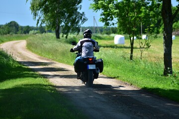 Motorcyclist rides an adventure touring motorcycle on a gravel countryside road. Rural landscape...