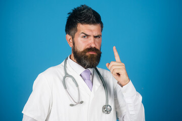 Serious male doctor in white coat with stethoscope raising finger up giving advice, recommendations...