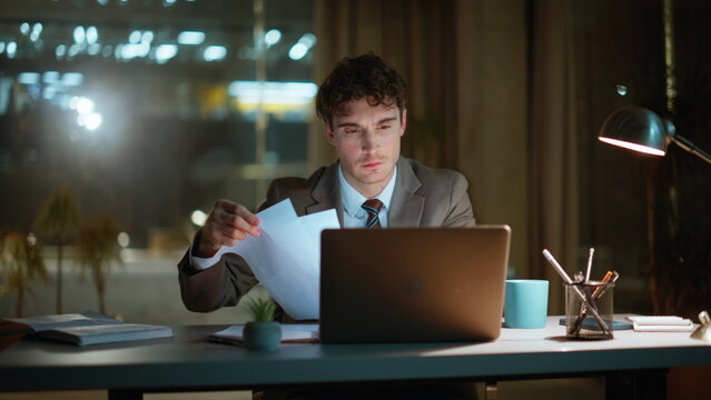 Focused manager doing paperwork at night office closeup. Smiling man rejoicing