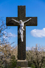 Beautiful Jesus Christ on crucifix, spring Easter budding tree flowers in background, cemetery on a sunny day, new life and religion concept